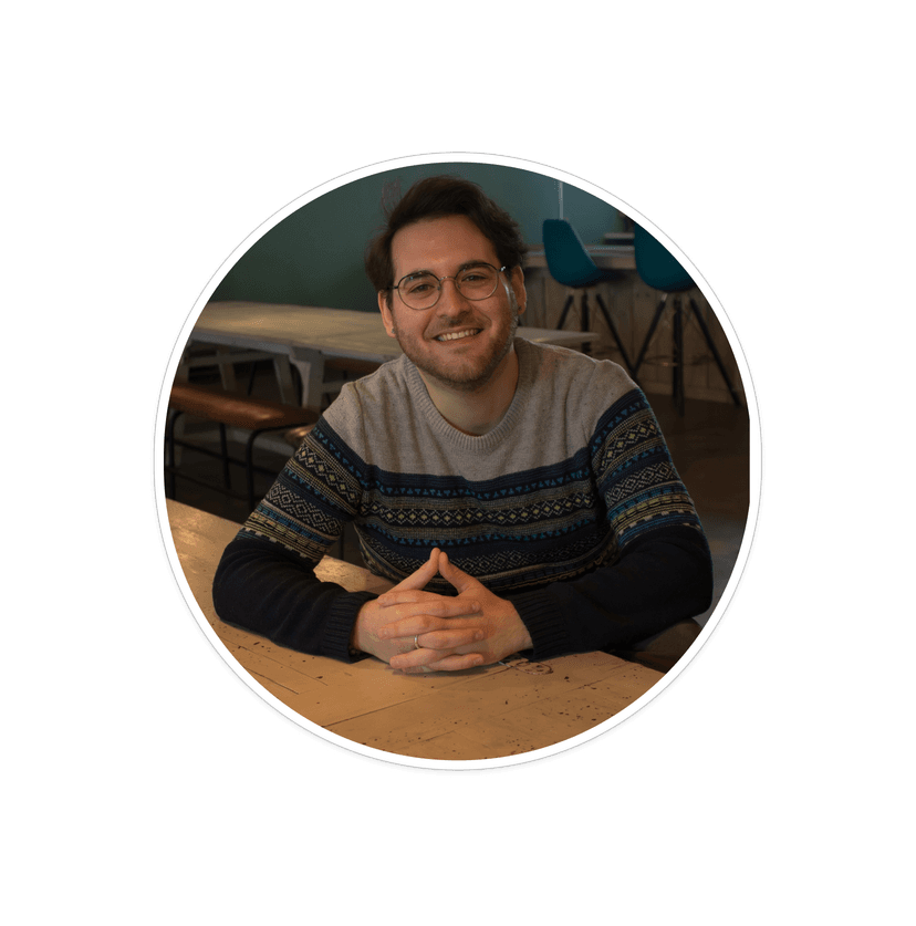 Manny sitting at a table with his hands held together, facing forwards, smiling.